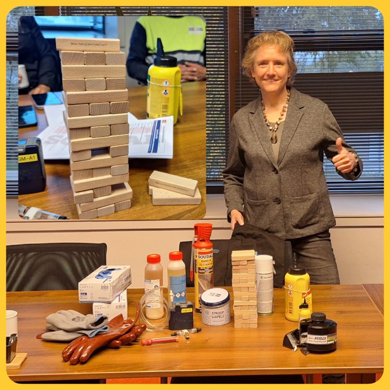 VGM Breed Nieuws - Imke Breedveld heeft trainersbevoegdheid ISOPA gehaald om mensen te trainen hoe veilig met diisocyaten te werken. Zij staat hier achter een tafel met daarop een aantal producten die diisocyanaten bevatten.